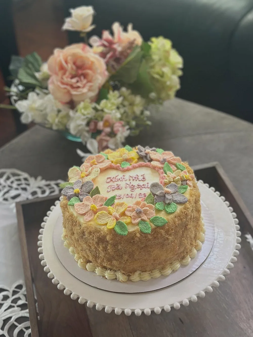 A salted egg sponge cake with pastel buttercream flowers, in front of a vase of fresh roses