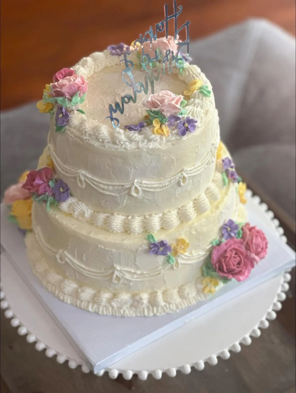 The two-tier cream flower cake from the side, showing the piped swags and buttercream roses